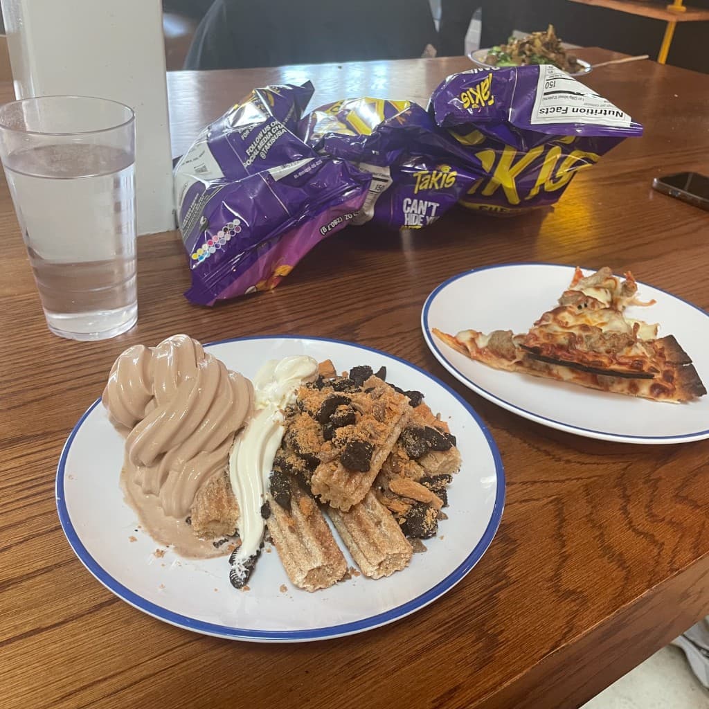 A table with churros, ice cream, pizza, Takis, and water