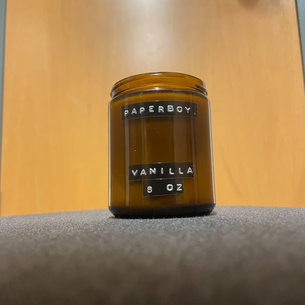 A brown glass candle jar labeled Paperboy Vanilla 8 oz